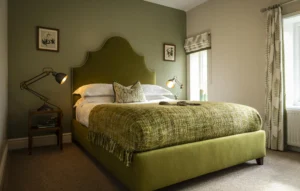 Stylish bedroom at Owl Cottage, Peplow Hall Estate, Shropshire, featuring a green upholstered bed, botanical décor and soft natural light in a luxury self-catering holiday cottage.